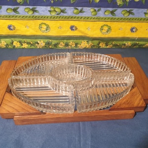 Peut inclure: Un plat de service en verre transparent avec quatre sections, séparées par des crêtes surélevées. Le plat est posé sur un plateau en bois avec une finition en bois naturel.