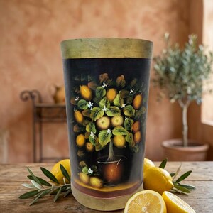May include: A cylindrical vase with a dark black background featuring a hand-painted illustration of a lemon tree in a pot, surrounded by green leaves and small white flowers, with a muted gold-toned rim and base border.