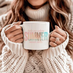 May include: White ceramic mug with the text "take me where SUMMER never ends" in pastel colors. The mug features a palm tree graphic and is held by a person wearing a cream-colored sweater.
