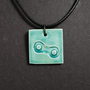 May include: A turquoise ceramic pendant necklace with a white chain link design. The pendant is square shaped and has a black cord.