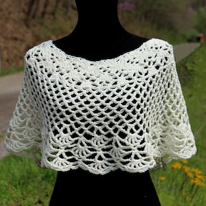 May include: A white crocheted shawl with a scalloped edge. The shawl is displayed on a black mannequin. The text "Krissys Over The Mountain Crochet" is visible in the top right corner of the image.