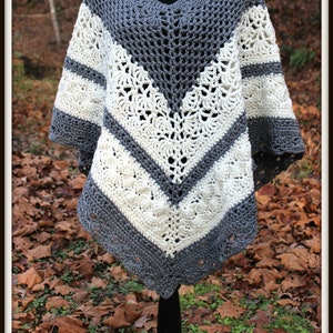 May include: Gray and white crochet poncho with a V-shaped design. The poncho is on a mannequin and has a fringe border.