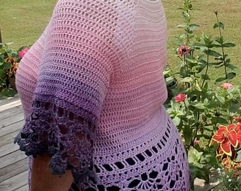 Pode incluir: Uma mulher vestindo um top de crochê com um degradê de rosa, roxo e cinza. O top tem uma borda de renda e é usado sobre uma saia preta. O texto "Krissys Over The Mountain Crochet" é visível na saia.