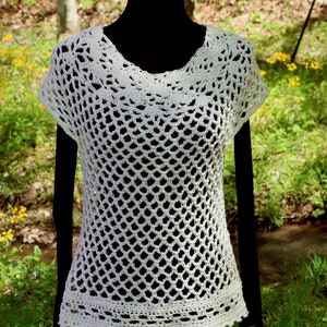 May include: White crochet top with a loose, open-weave design. The top has short sleeves and a scoop neckline. The bottom hem is finished with a crocheted border.