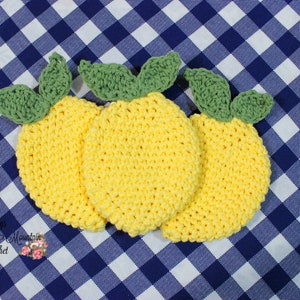 May include: Three crocheted lemon-shaped pot holders in yellow with green leaves. The pot holders are on a blue and white checkered tablecloth.