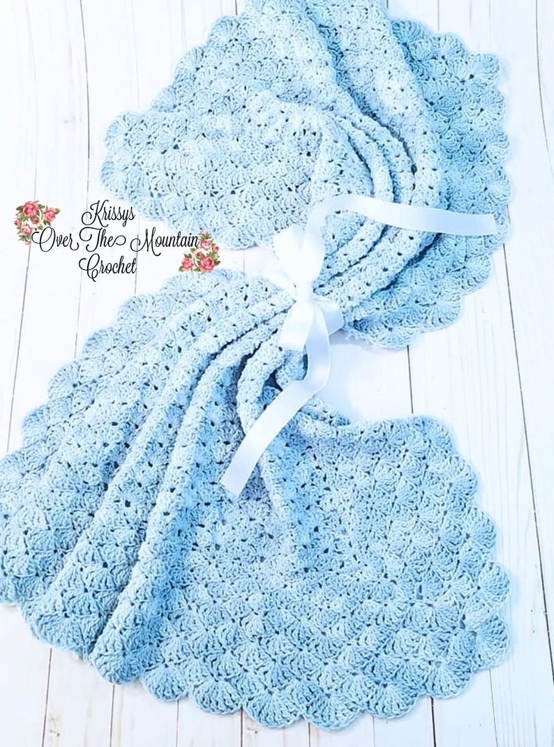 May include: A light blue crocheted baby blanket with a scalloped edge. The blanket is tied with a white satin ribbon. The text "Krissys Over The Mountain Crochet" is visible in the image.