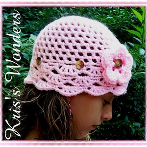 May include: A pink crocheted hat with a flower embellishment and buttons. The hat has a scalloped edge and is made with a delicate open stitch pattern.