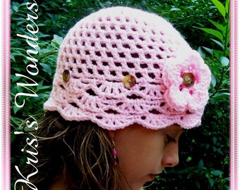 May include: A pink crocheted hat with a flower embellishment and buttons. The hat has a scalloped edge and is made with a delicate open stitch pattern.