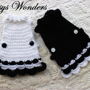 May include: Two crocheted baby dresses, one white with black trim and one black with white trim. Both dresses have a scalloped hem and black buttons.