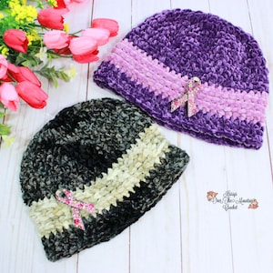 May include: Two crocheted beanies made of soft velvet yarn. One beanie is deep purple with a lighter purple band, and the other is dark charcoal with a light gray band. Each hat features a pink rhinestone ribbon pin attached to the center band.