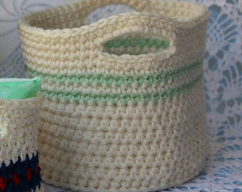 May include: A white crocheted basket with a green stripe around the middle. The basket has a handle on the top.