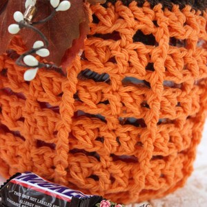 May include: Orange crochet pumpkin-shaped container with a brown crocheted top. The container is filled with candy bars. The text on the candy bar wrapper reads: "THIS UNIT NOT LABELED FOR RETAIL ALLERGY INFORMATION: CONTAINS PEANUTS, MILK, EGG AND SOY. MAY CONTAIN TREE NUTS."