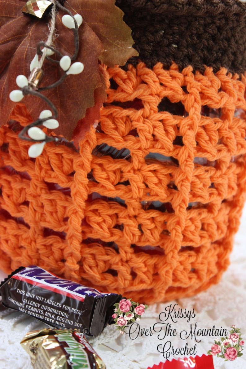 May include: Orange crochet pumpkin-shaped container with a brown crocheted top. The container is filled with candy bars. The text on the candy bar wrapper reads: "THIS UNIT NOT LABELED FOR RETAIL ALLERGY INFORMATION: CONTAINS PEANUTS, MILK, EGG AND SOY. MAY CONTAIN TREE NUTS."