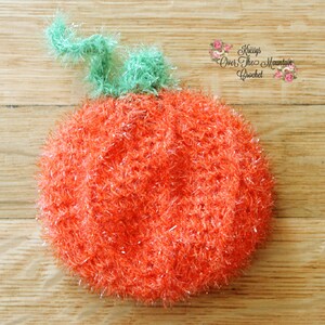May include: A crocheted orange pumpkin with a green stem. The pumpkin is made with sparkly yarn and has a fuzzy texture.