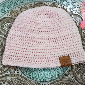 May include: A pink crocheted beanie with a brown leather tag that says "stitched with LOVE".
