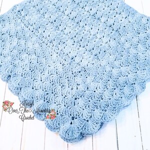 May include: A light blue crocheted baby blanket with a scalloped edge. The blanket is made with a textured stitch pattern and has a subtle ombre effect.
