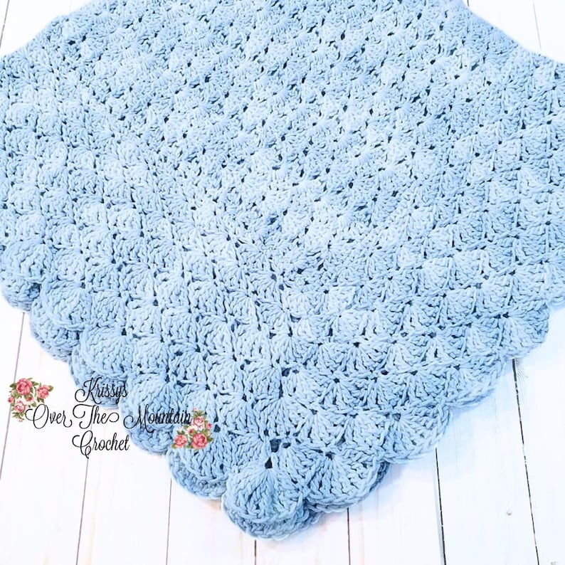 May include: A light blue crocheted baby blanket with a scalloped edge. The blanket is made with a textured stitch pattern and has a subtle ombre effect.