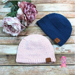 May include: Two crocheted hats, one pink and one blue, with leather labels. The pink hat has a label that says "Handmade with LOVE" and the blue hat has a label that says "Kisses On The Mountain Crochet".