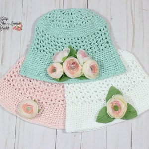 May include: Three crocheted sun hats in different colours: mint green, pink and white. Each hat has a flower embellishment.