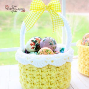 Könnte beinhalten: Ein handgefertigter, gelber Häkel-Osterkorb mit weißem, gewelltem Rand und Henkel. Der Korb ist mit verzierten Ostereiern gefüllt. Eine gelb-weiß karierte Schleife ziert die Oberseite. Der Text "Krissy's Over The Mountain Crochet" ist sichtbar.