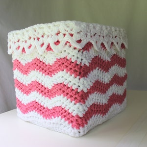 May include: A pink and white crocheted storage basket with a white crocheted lace trim. The basket is made in a chevron pattern.