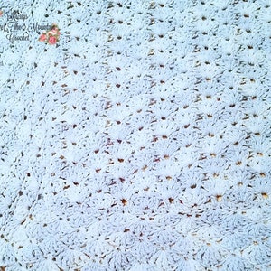 May include: A close-up of a light blue crocheted blanket with a repeating pattern of small flowers. The blanket is made with a soft, fluffy yarn.