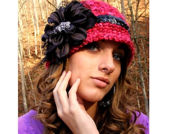 May include: A red crocheted hat with a black flower and a black ribbon. The hat has a wide brim and is decorated with sequins.