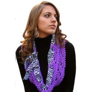 May include: Purple crocheted infinity scarf with a zebra print fabric accent. The scarf is worn by a person with long brown hair.