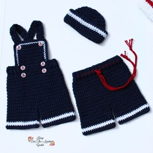 May include: A crocheted sailor outfit for a baby, featuring a blue and white striped hat, blue overalls with white trim and anchor buttons, and blue shorts with white trim and a red drawstring.