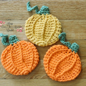 May include: Three crocheted pumpkins, one yellow, two orange, with green stems. The pumpkins are on a wooden surface.