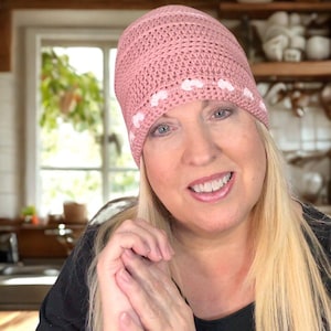 Könnte beinhalten: Ein rosa gehäkelter Beanie mit weißen Tupfen. Der Hut ist handgefertigt und wirkt weich und bequem. Das Bild enthält auch den Text "Krissy's Over The Mountain Crochet".