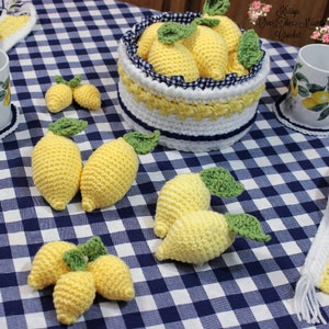 May include: Crocheted lemon decorations on a blue and white checkered tablecloth. The lemons are in a basket, on a coaster, and on the table. The text "Kissys Over The Mountain Crochet" is visible in the image.