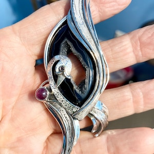 May include: A silver pendant featuring a black agate stone with a detailed bird design. The bird has a ruby red eye and a ruby red stone on its chest.