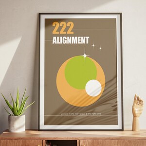 May include: A framed poster with a brown background and the text "222 ALIGNMENT" in white. The poster features a large orange and green circle with a smaller white circle inside. The text "You are in the right place & the right time" is at the bottom of the poster.