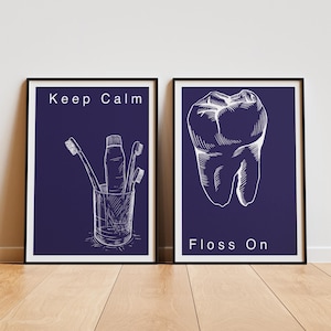 Könnte beinhalten: Zwei gerahmte Drucke mit einem marineblauen Hintergrund und weißem Text. Der linke Druck sagt "Keep Calm" und zeigt eine Zeichnung von Zahnbürsten und Zahnpasta in einem Glas. Der rechte Druck sagt "Floss On" und zeigt eine Zeichnung eines Zahns.