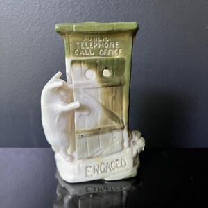May include: A novelty ceramic figurine depicting a pig at a public telephone box. The box is painted in cream and green, with the words "PUBLIC TELEPHONE CALL OFFICE" and "ENGAGED". A charming and quirky decorative piece.