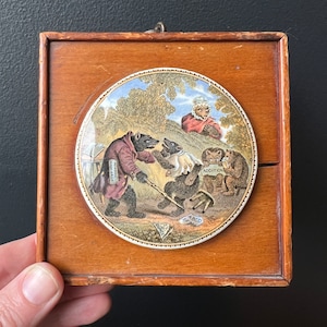 Puede incluir: Un azulejo de cerámica enmarcado con una ilustración colorida de tres osos y un gato. Los osos llevan ropa y sostienen un libro y un cartel que dice "Addition". El azulejo está rodeado por un marco de madera.