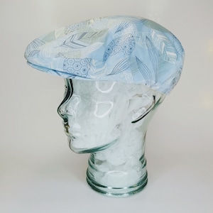 May include: A light blue patterned cap with a white background and a design of leaves and circles. The cap is on a glass head form.