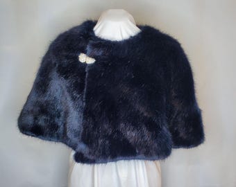 Peut inclure: Une cape en fausse fourrure bleu marine, fermée par un fermoir décoratif en strass. La cape est présentée sur un mannequin blanc. La fausse fourrure a un aspect doux et texturé. Un accessoire élégant pour les occasions spéciales.