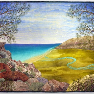 Puede incluir: Una obra de arte acolchada que representa una escena de paisaje con un océano azul, una playa de arena, un campo de hierba verde y un río azul sinuoso. La escena está enmarcada por dos árboles a cada lado de la imagen.