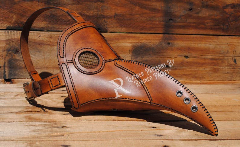 May include: A brown leather plague doctor mask with a long beak and a mesh eye covering. The mask has a strap that goes around the head and is decorated with stitching and eyelets. The text "Leather Patterns By Refined Parfait" is printed on the mask.
