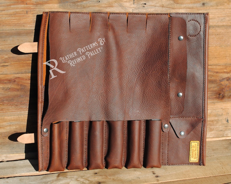 May include: A brown leather tool roll with multiple pockets and a flap closure. The roll features a series of vertical pockets for holding tools, and a strap with a buckle to secure the roll. The text "Leather Patterns by Refined Pallet" is visible.