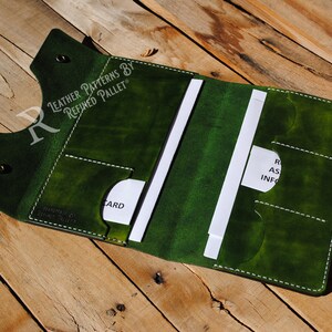 May include: A green leather wallet with white stitching and multiple card slots. The wallet is open and has a white card inside. The text "LEATHER PATTERNS BY REFINED PALLET" is embossed on the front of the wallet.