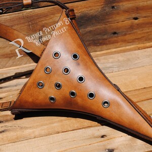 May include: A brown leather plague doctor mask with a long, pointed beak and multiple eyelets. The mask is attached to a brown leather strap. "Leather Patterns by Refined Pallet" is written on the strap.