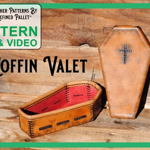 May include: A leather coffin-shaped valet box with a red interior and a cross design on the lid. The box is made of brown leather and has a stitched edge. The text "Coffin Valet" is visible in the image.