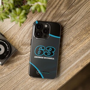 May include: Black phone case with a blue and white design. The case features the number "63" and the name "George Russell". The Mercedes-Benz logo and Petronas branding are also visible.