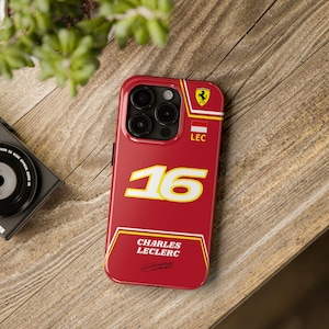 May include: Red and yellow iPhone case with a Ferrari logo, the number 16, and the name Charles Leclerc.