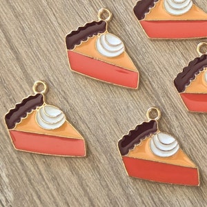 May include: Ten gold-tone metal charms shaped like pumpkin pie slices with brown crust and white whipped cream. The charms have a shiny finish and are perfect for jewelry making or crafting.