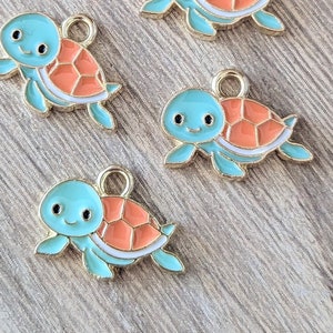 May include: Five gold-colored turtle charms with blue bodies and orange shells. The turtles have white outlines and black eyes.