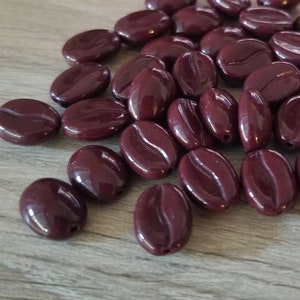 May include: A pile of dark brown coffee bean shaped beads. The beads are made of plastic and have a glossy finish.